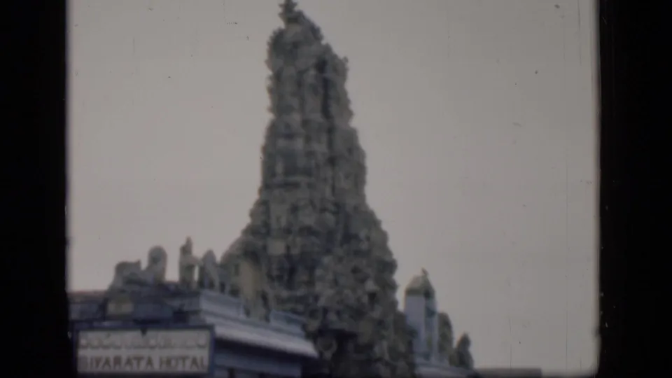 1946 Bombay 8mm frame showing the temple tower framed higher against pale sky above surrounding buildings.
