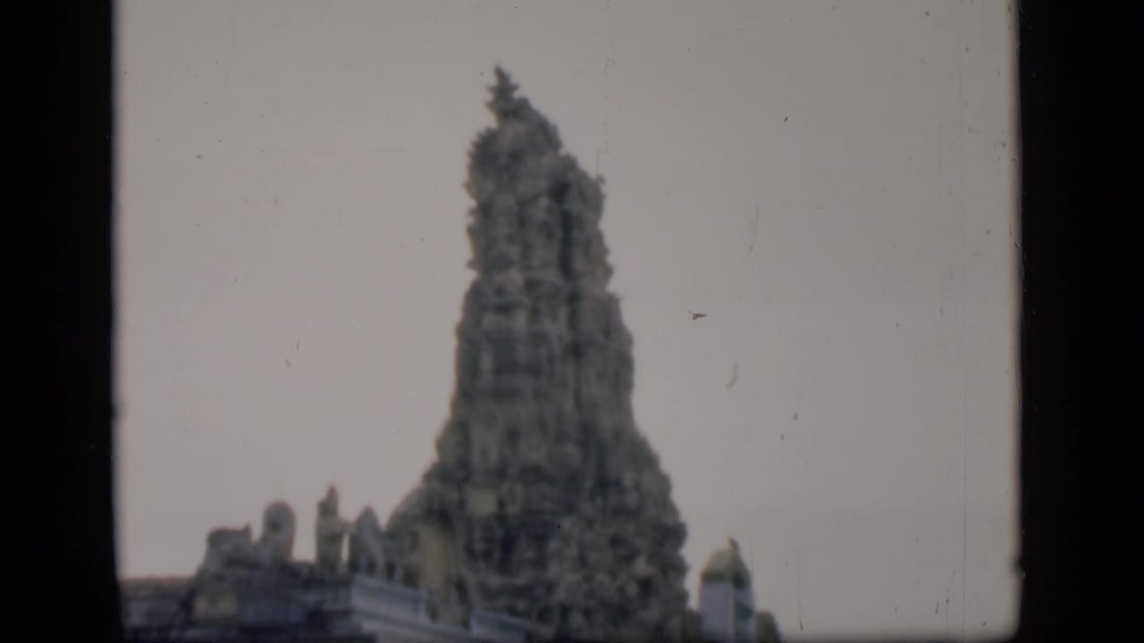 Distant view of an ornate temple tower against a pale sky with film-frame borders.