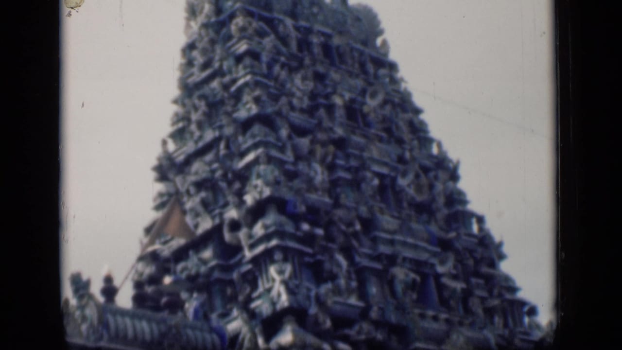 Ornately carved temple tower seen against a pale sky with dark film borders.