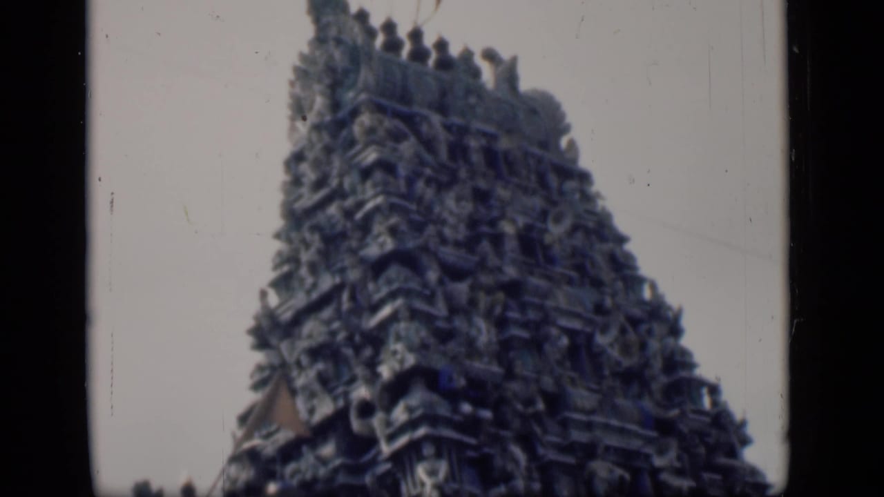 Similar view of a carved temple tower with sculptural tiers and sky behind it.