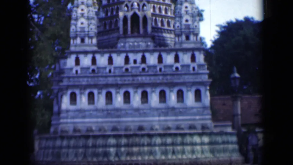 1946 Bombay frame showing the temple facade and gopuram, with rows of arches, sculptural ornament, and surrounding trees.
