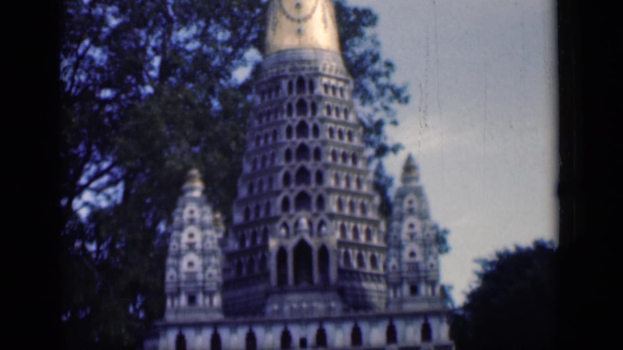 1946 Bombay 8mm frame showing an ornate temple tower with arched tiers, a gold-toned spire, trees, and smaller side towers.
