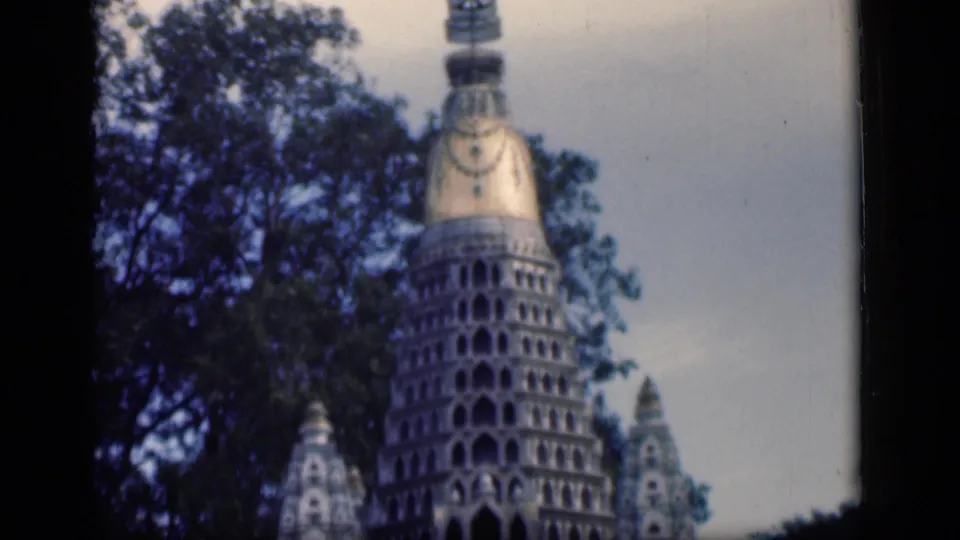 1946 Bombay 8mm frame showing the ornate temple tower cropped close, with repeated arches, gold-toned spire, trees, and sky.