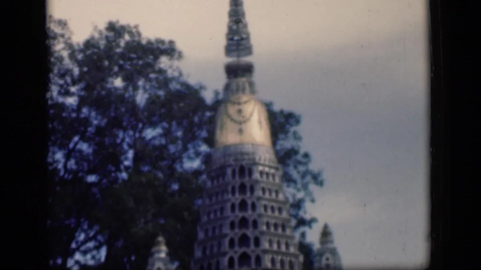 1946 Bombay 8mm frame with the temple's gold-toned spire and upper tiers partly framed by dark trees and pale sky.