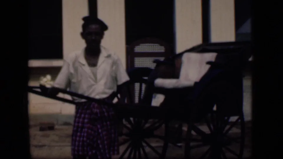 1946 Bombay frame showing a man in a white shirt and checked garment beside a rickshaw outside a building.