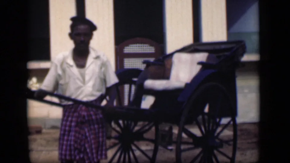 In Bombay, India, a rickshaw driver stands holding the poles of a hand-pulled rickshaw in 1946 home-movie footage.