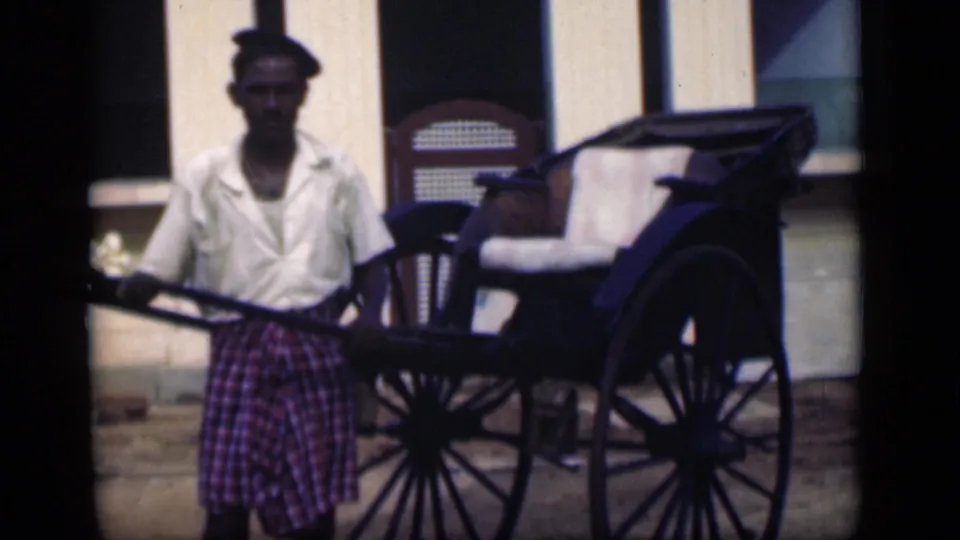 A man stands with a traditional rickshaw in Bombay, India, framed by building windows in 1946 8mm footage.