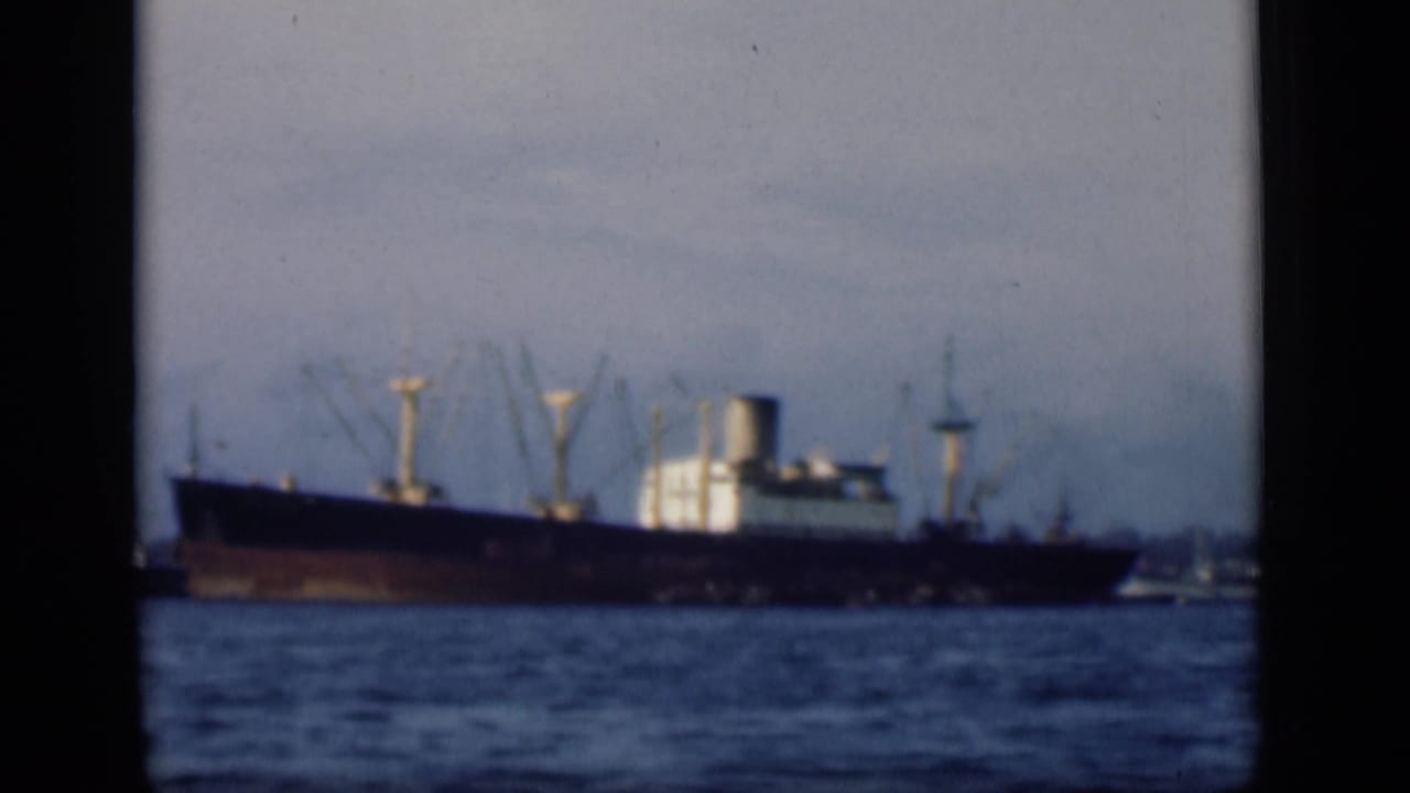 A distant cargo ship sits on harbor water in likely Bombay, India, in 1946 8mm home-movie footage.