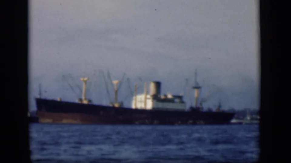 A distant cargo ship sits on harbor water in likely Bombay, India, in 1946 8mm home-movie footage.