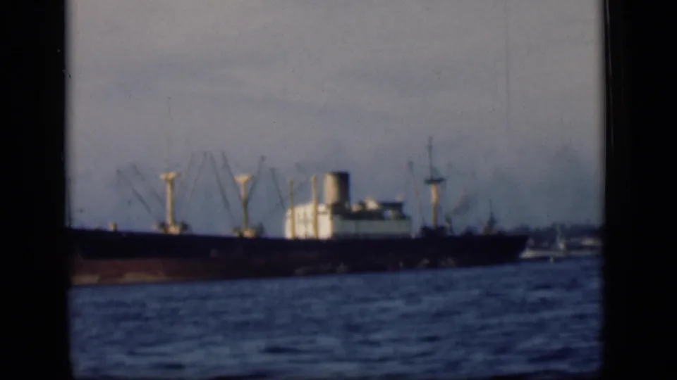 The cargo ship remains in distant view on harbor water, softened by 8mm focus and visible film borders.