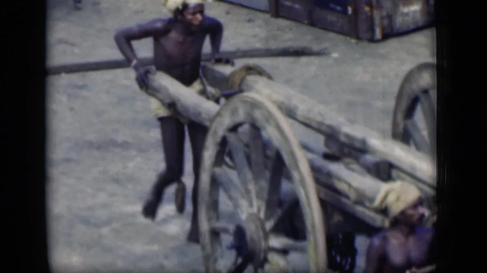 A worker in Bombay, India, 1946 appears to push or steady a heavy wooden cart as another man is partly visible nearby.
