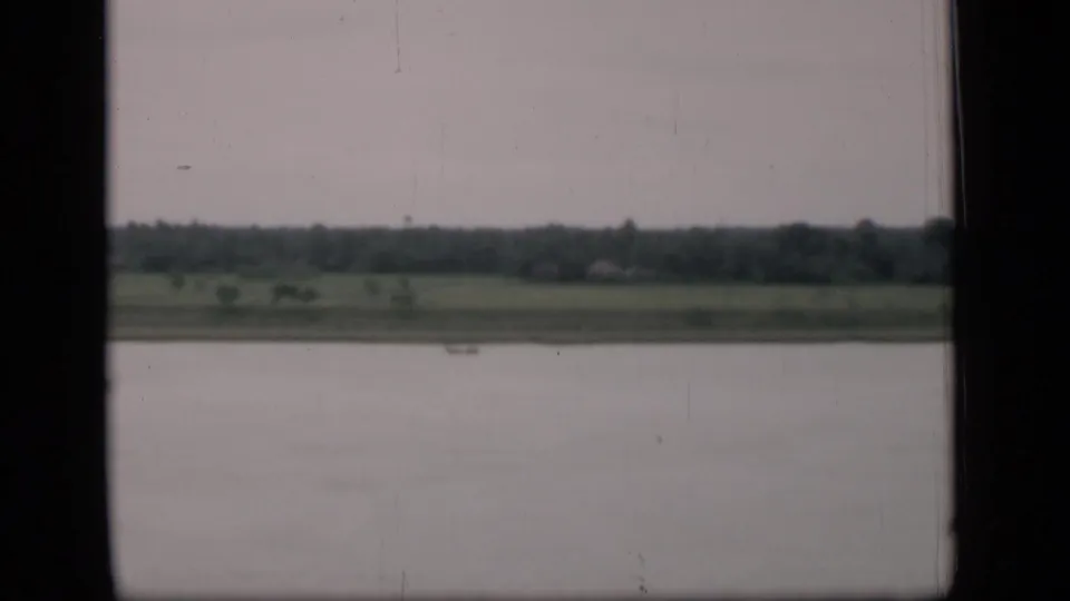 1946 Bombay riverside view with muted water, far green shoreline, distant trees, dark porthole-like edges, and visible film wear.