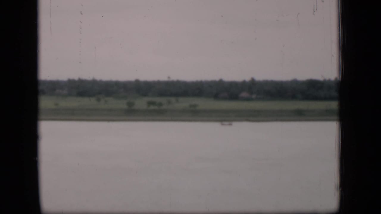 Broad water surface, green bank, distant trees, and a small boat framed by window edges.