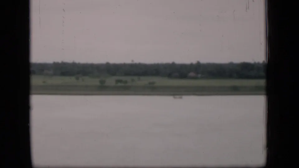 A muted 1946 Bombay landscape shows calm water, a narrow green bank, distant trees, and a small boat through a dark window frame.