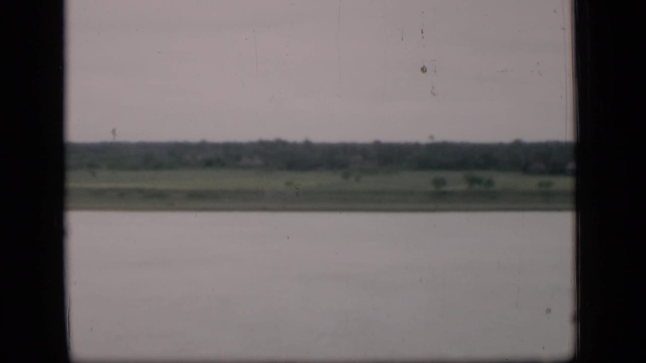 Calm waterway with distant green shoreline under a cloudy sky, framed by dark vertical edges.