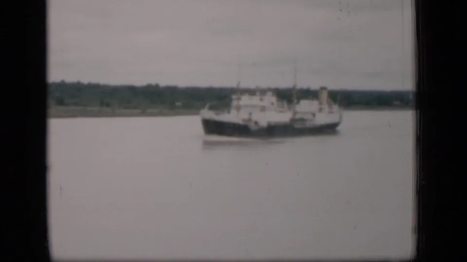 1946 Bombay home-movie frame showing a cargo ship on calm water beneath a pale sky, with shoreline in the distance.