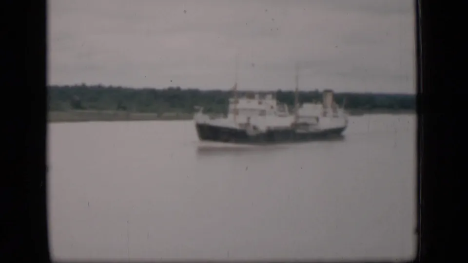 The vessel remains in view on calm water in this 1946 Bombay frame, with a soft horizon and trees behind it.
