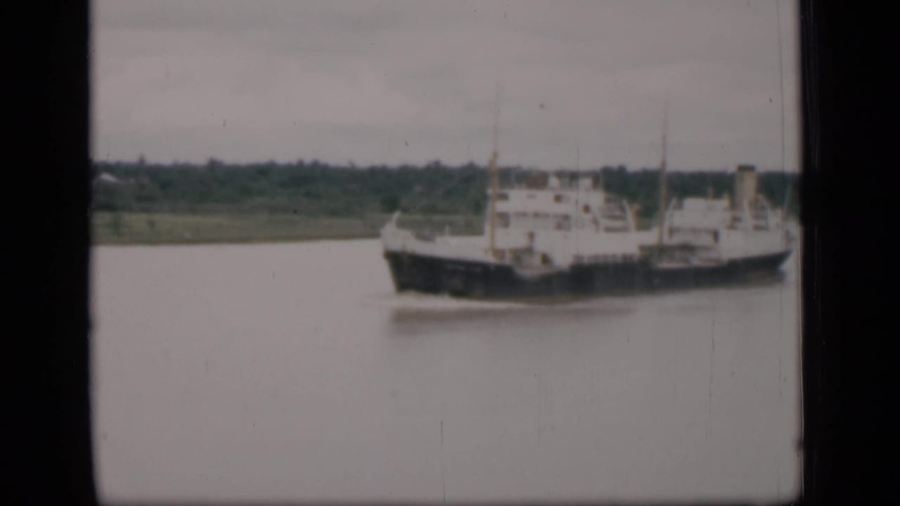 Cargo vessel traveling on calm river water near a low shoreline.