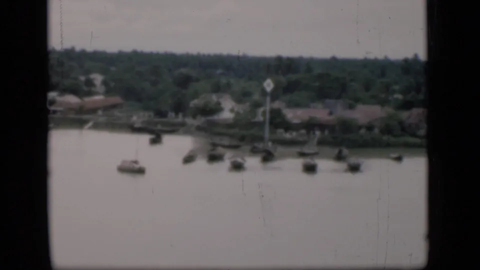 A second wide frame shows boats scattered across calm water, with trees and low riverside structures beyond in Bombay archival footage.