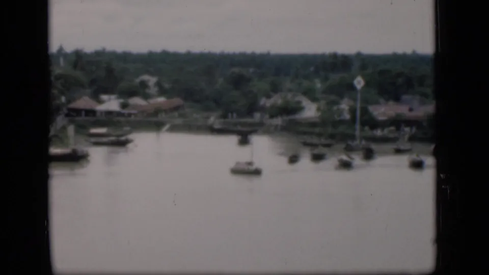 1946 Bombay river view with boats near the far bank, low houses, lush vegetation, and a tall pole or marker.