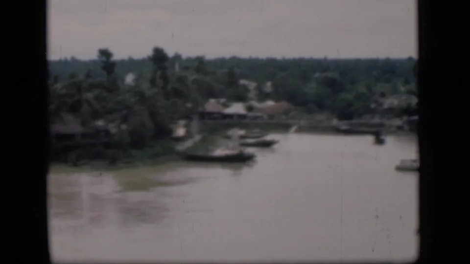 1946 Bombay riverbank view showing a muddy shoreline, small boats, low houses, and tropical vegetation.