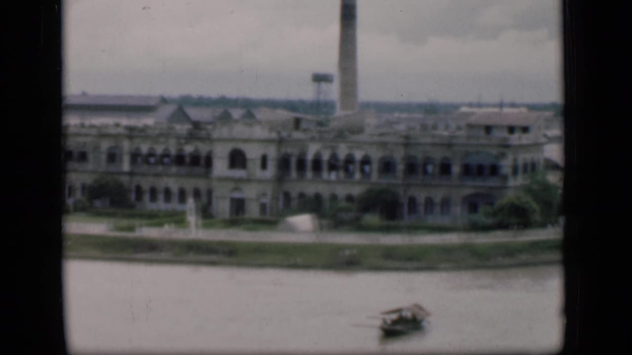 Riverfront building with arched windows, smokestack, and small boat on the water.