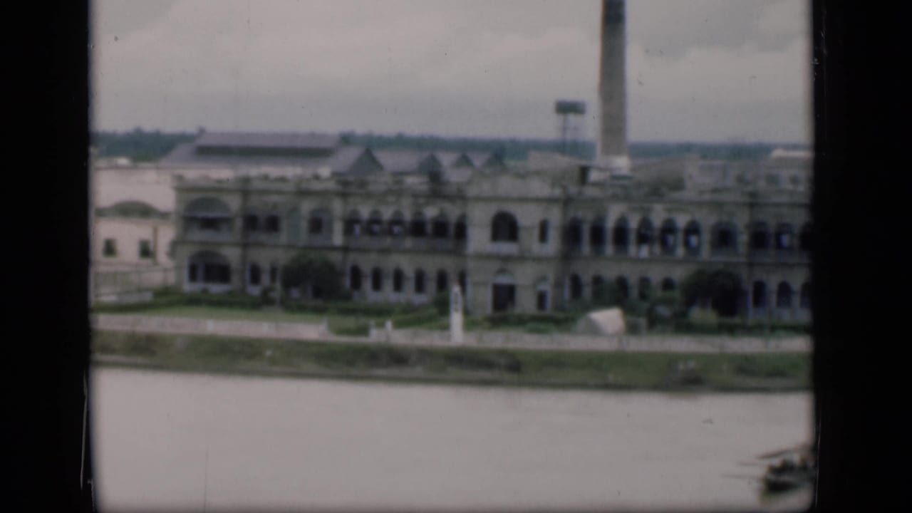 Bombay waterfront pan showing the arched riverfront structure, tall smokestack, open water, and a small boat at the lower right.