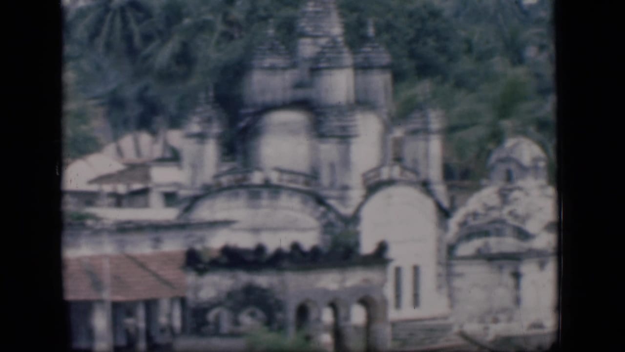 1946 Bombay 8mm frame showing a whitewashed domed historic complex with spires, arched walls, and tropical greenery.