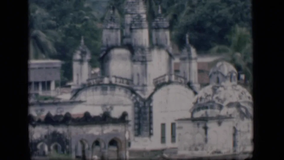 1946 Bombay frame showing a white domed landmark with spires, arched masonry, palms, and low buildings at the edges.