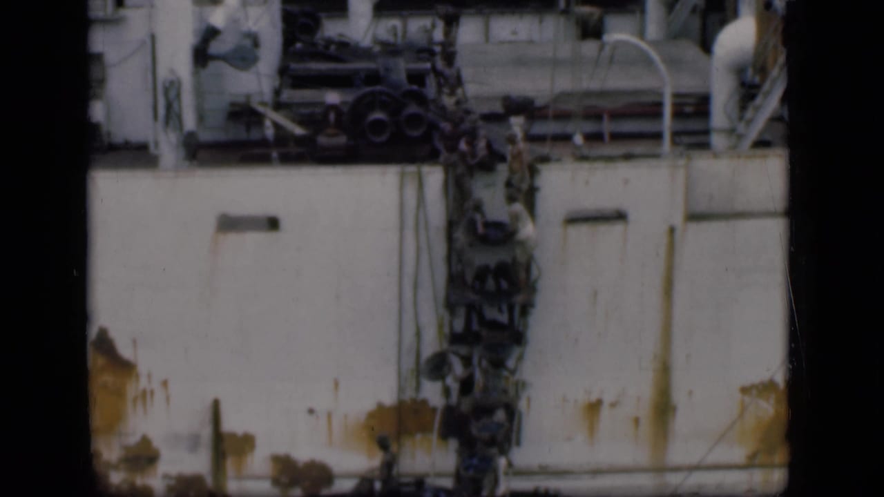 Workers clustered along the side of a white vessel near pipes and machinery.