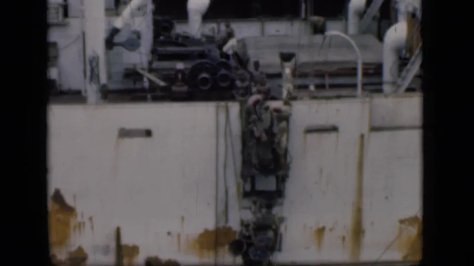 1946 Bombay home-movie frame showing workers positioned against a large vessel hull below pipes, railings, and shipboard machinery.
