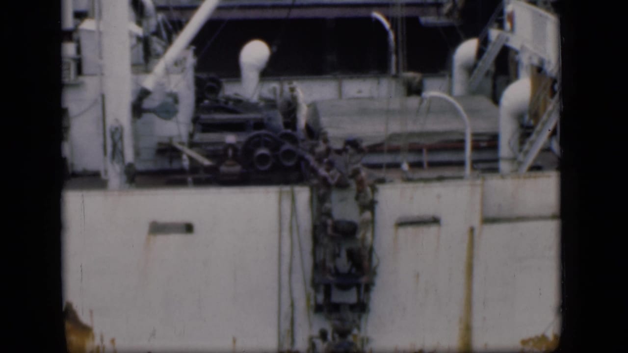 People appear to move up or down a ladder on the side of a ship in Bombay, with railings and deck fixtures visible above.