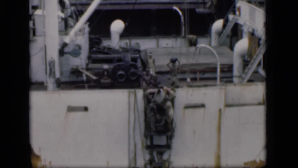 A close home-movie view of people near a ladder on a large ship, with the vessel's pale side and deck details filling the frame.