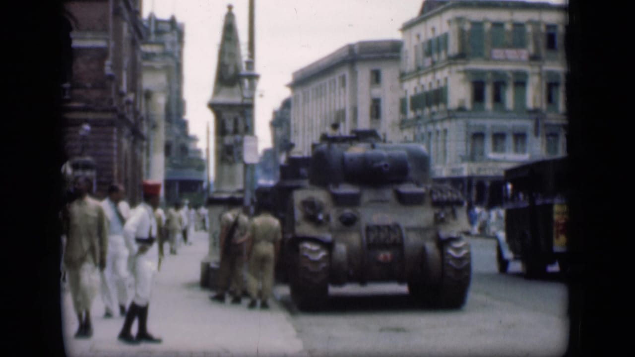 Uniformed men and pedestrians stand near a tank on a busy city street.