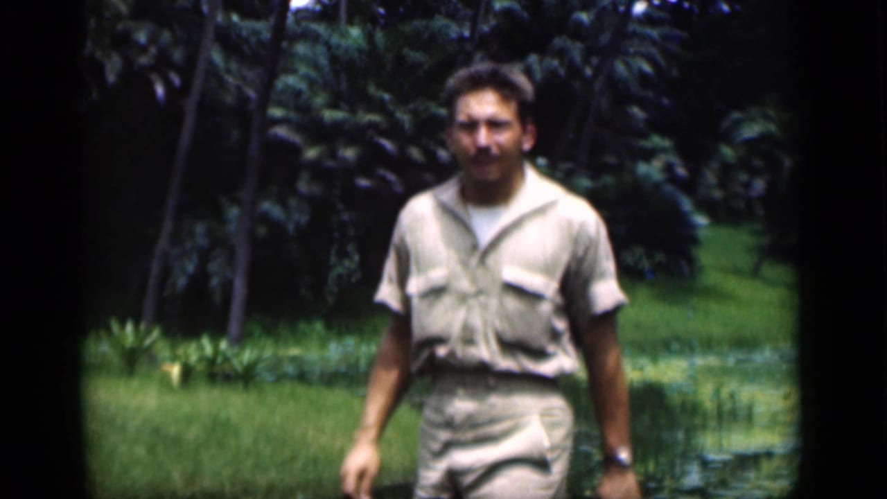 Adult man walking through a green tropical park toward the camera.