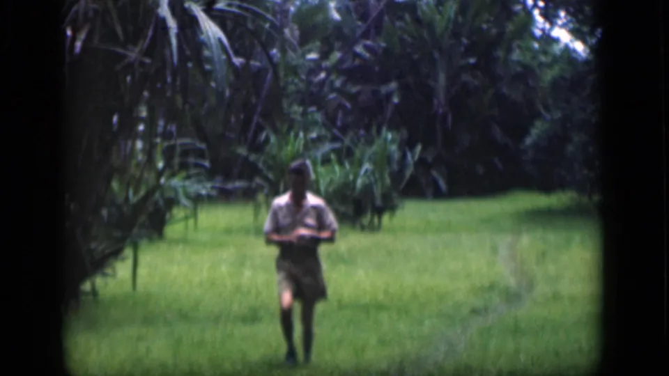 Adult man walks toward the camera through a lush field in Bombay, India, in 1946 home-movie footage.