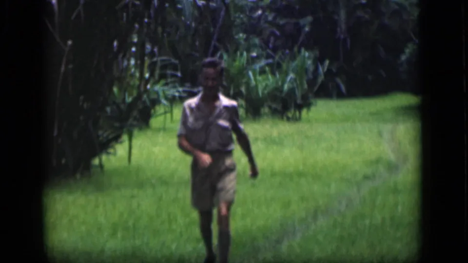 Adult man walks toward the camera through a green field in supported 1946 Bombay home-movie footage.