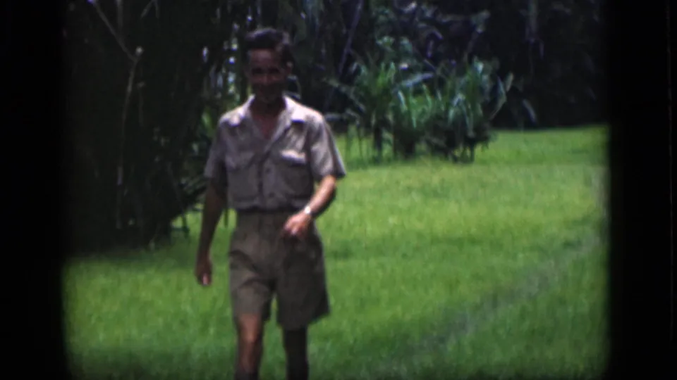 Closer 1946 Bombay frame showing an adult man in a light shirt and shorts walking through tropical grass.