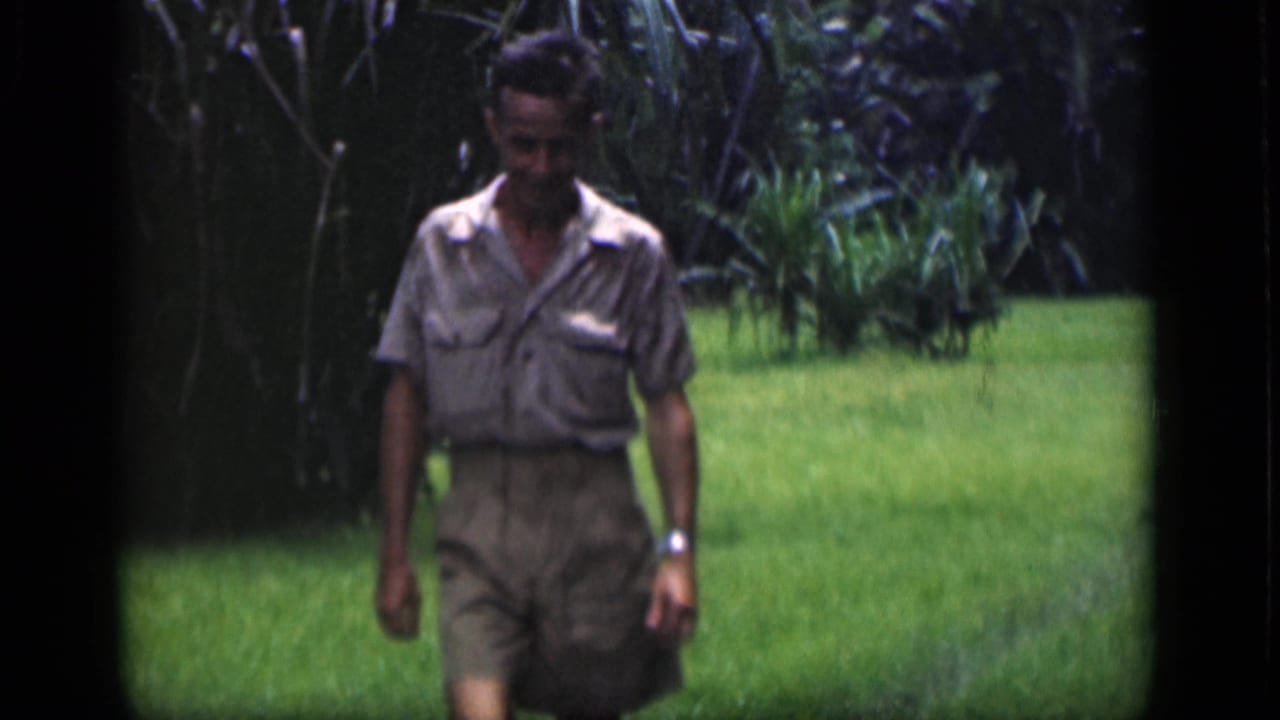 Adult man in a light shirt and shorts walking across a grassy garden.