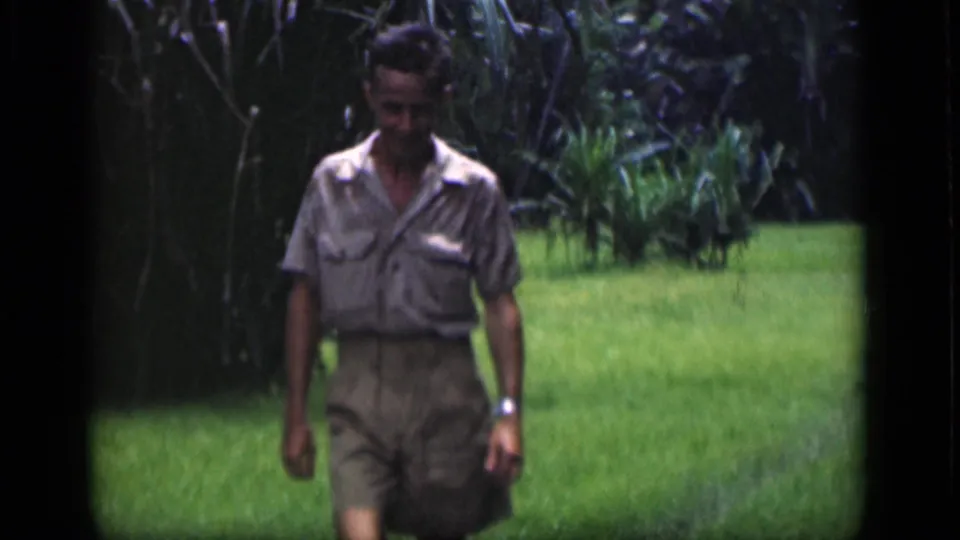 Adult man walks through a lush Bombay garden in 1946, partly shaded by dense tropical foliage.