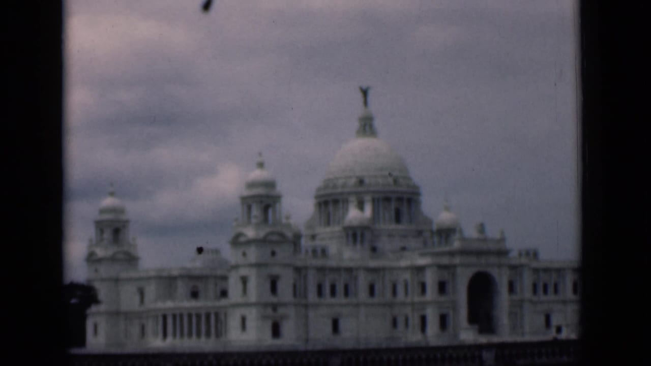Large white domed building seen beyond a dark vertical frame edge and cloudy sky.