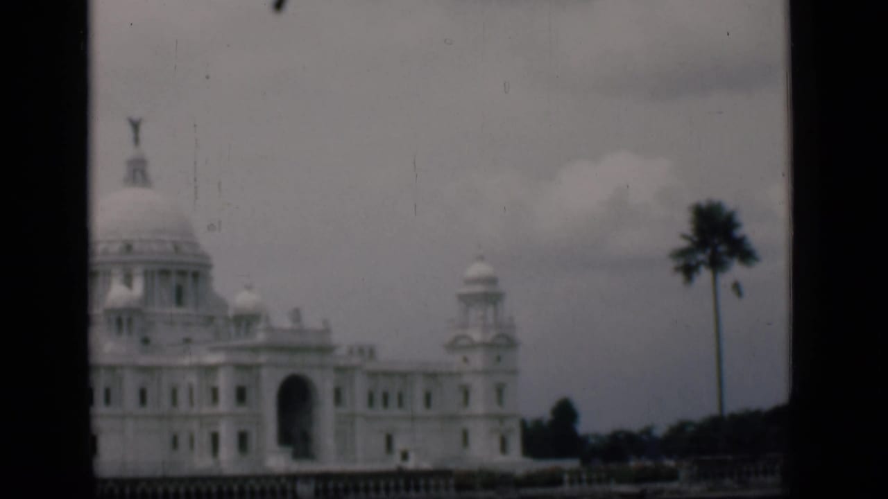 Domed white building with central arch, palm tree at right, cloudy sky, and dark vertical divider.