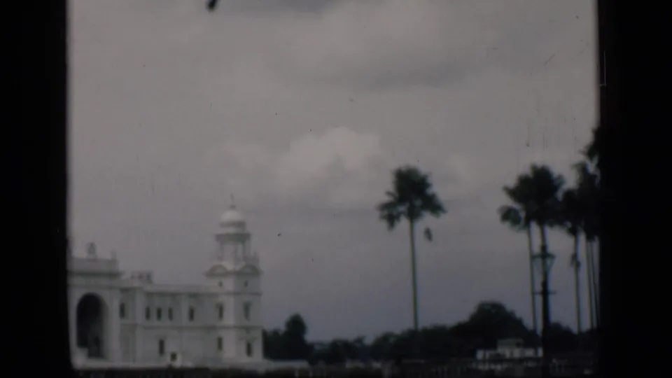 1946 8mm view identified as Bombay, India, showing a white landmark building partly framed by palms and dark window edges.