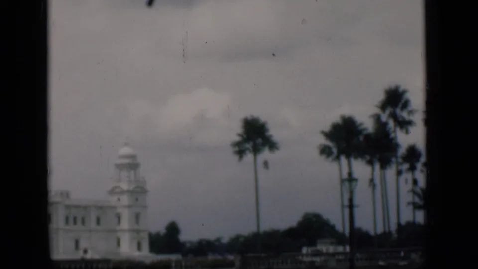 1946 8mm travel frame identified as Bombay, with a white towered landmark, palms, and cloudy sky seen from a framed viewpoint.