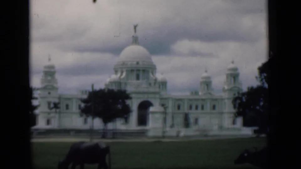 Final 1946 8mm frame identified as Bombay, with the domed white landmark, open lawn, cloudy sky, and cow in the foreground.