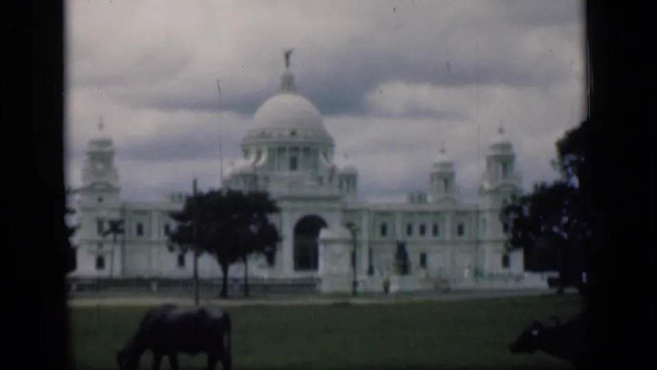 1940s 8mm view of the Victoria Memorial across a green lawn, with cloudy sky and water buffalo in the foreground.