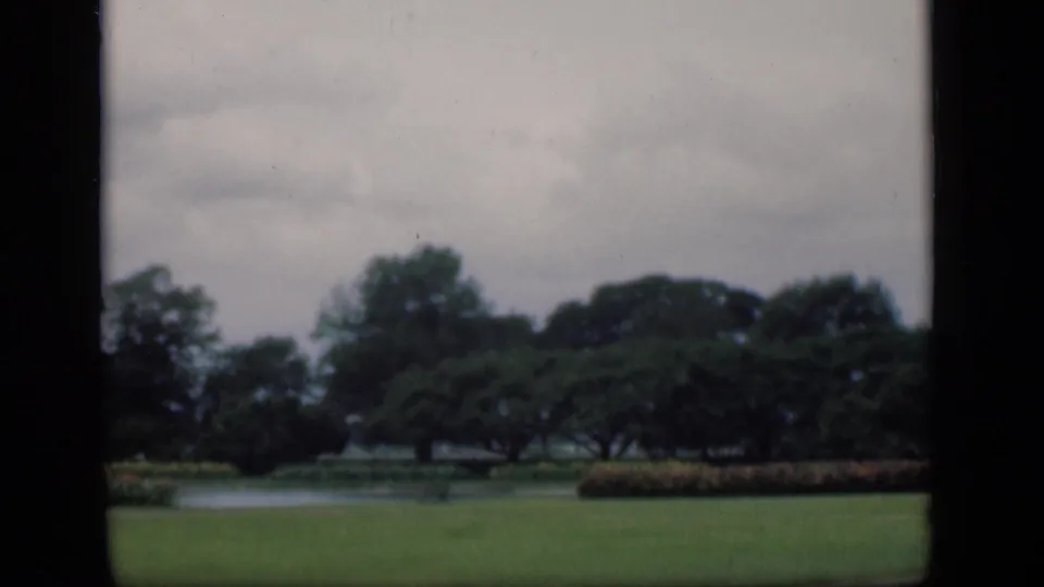 A soft 8mm view of a Bombay park in 1946, with open grass, pond water, hedging, and trees.