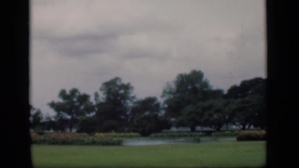 Bombay garden scene on 8mm film, showing a clipped lawn, pond, flowerbeds, and trees with muted color.