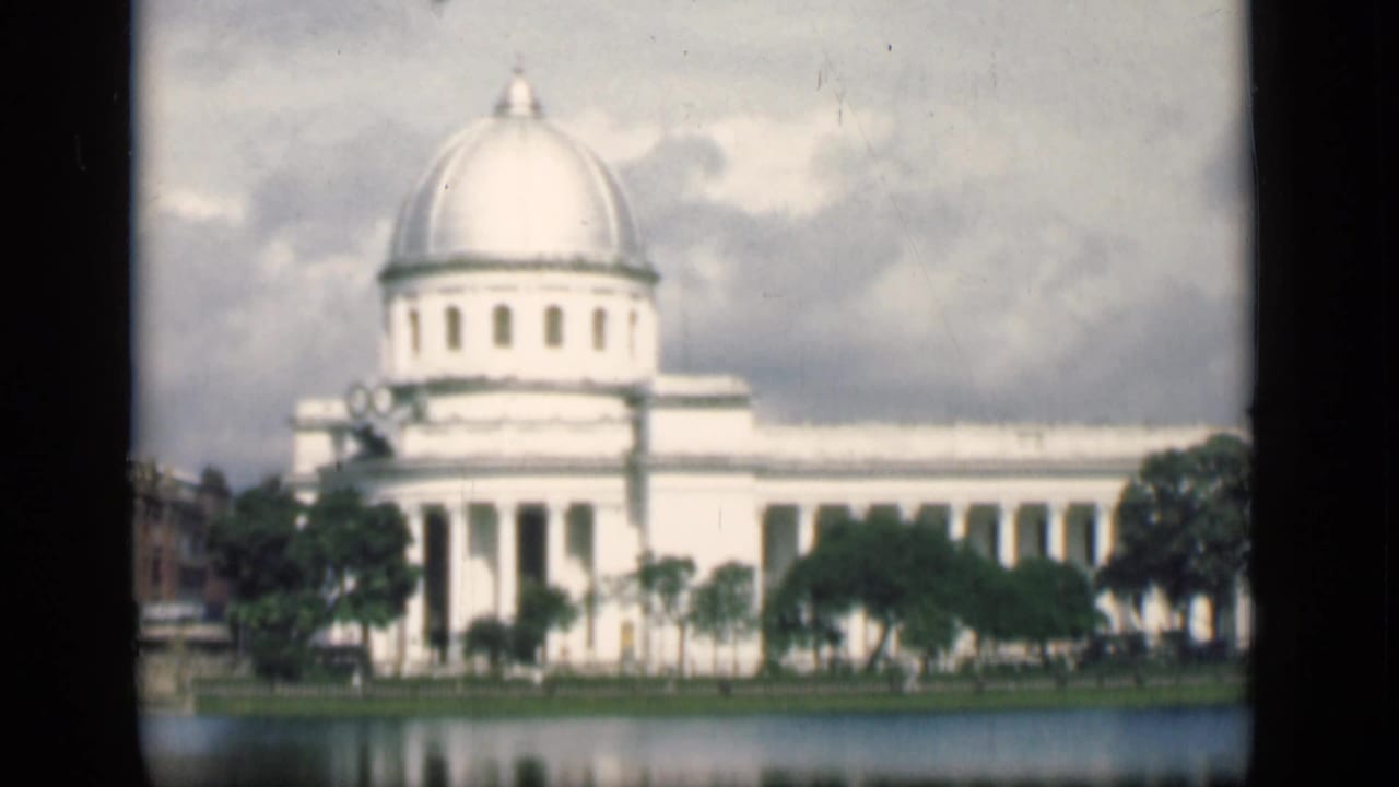 1946 Bombay frame of a large white domed building with columns, trees in front, and reflections in nearby water.