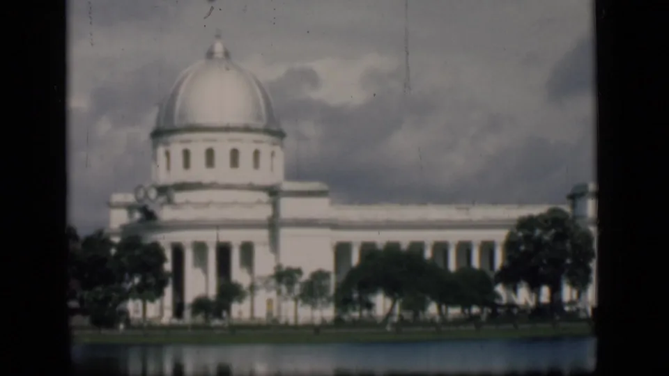 1946 Bombay home-movie view holding on a white domed landmark-like building, trees, cloudy sky, and water reflection.
